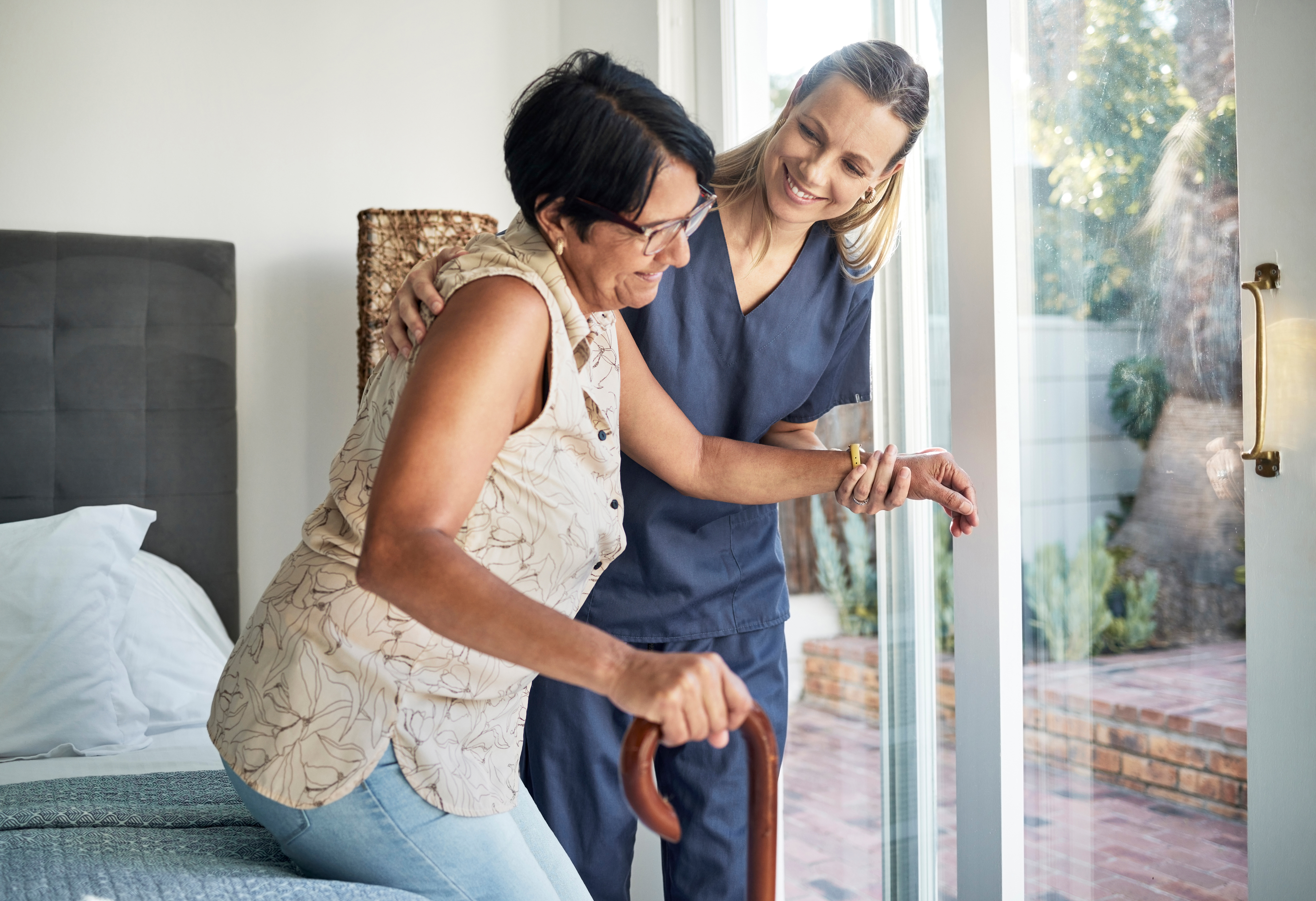Woman support worker helping older woman up from bed.