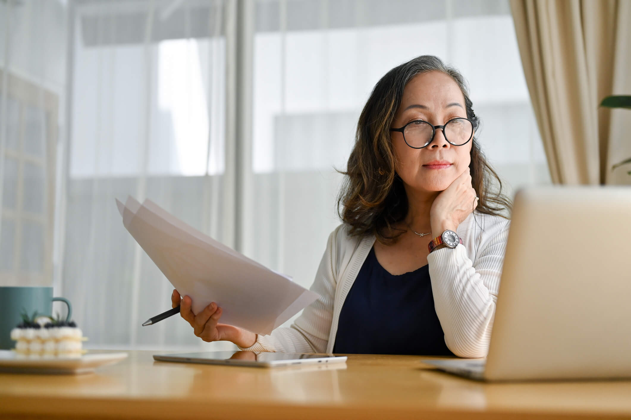 Woman holding papers looking at laptop