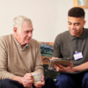 Young man showing ipad with care plan notes to old man